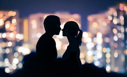 A man and woman in silhoette facing each other with coloured lights behind 